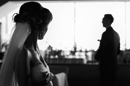 Bride looks at fiance who is standing in the front of the windowの写真素材