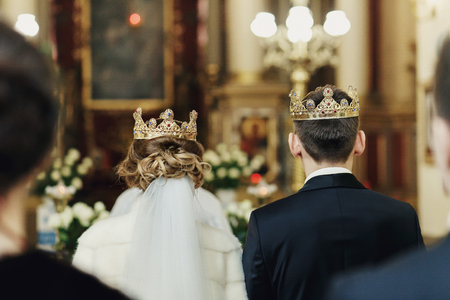 View on the backs of newlyweds in crowns from the crowd in churchの写真素材