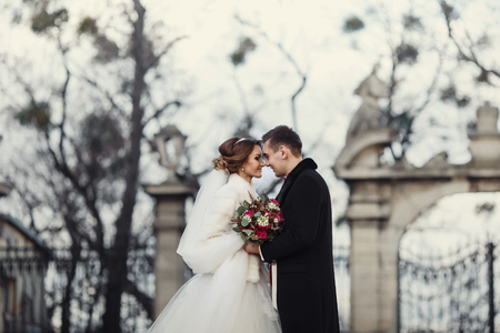Newlyweds posing in the front of old park gates in the cold weatherの写真素材