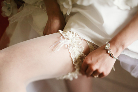 Bride adjusts a lace garter on a stockingの写真素材