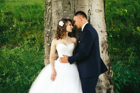 Man holds bride's waist tenderly behind a treeの写真素材