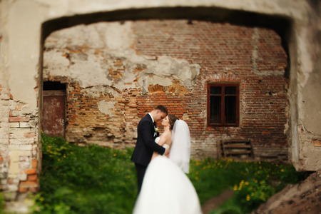 Groom holds bride tightly while standing in the front of brick wallの写真素材