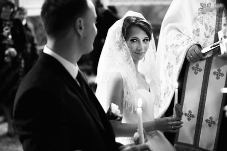 Bride covered with lace kerchief looks at the fiance during the ceremonyの写真素材