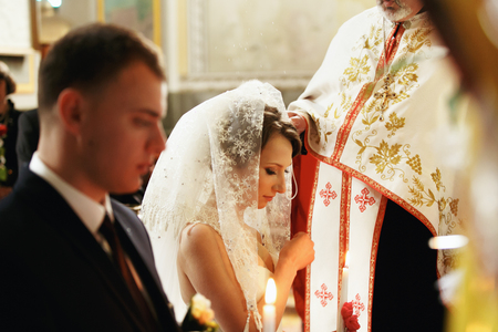 Bride in veil stands on the knees before a priestの写真素材