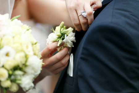 Delicate bride's hands pin a boutonniere in groom's jacketの写真素材