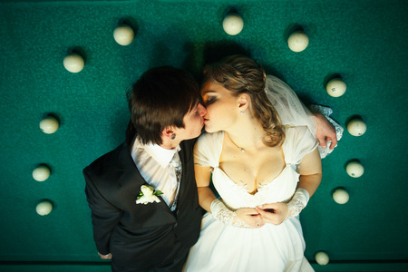 Couple kisses on the billiard table surrounded with white balls
