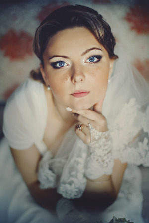 Blue-eyed blonde bride looks up while sits on the old sofaの写真素材