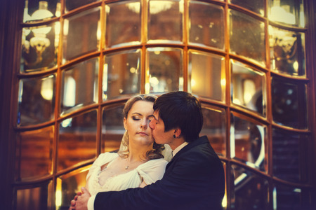 A delicate kiss of the groom to the bride in the front of old stained-glass windowの写真素材