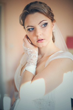 Bride looks thoughtful while adjusting her earrings in the rays of morning sunの写真素材