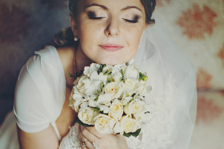 Bride smiles with closed eyes holding her chin on the bouquet of rosesの写真素材