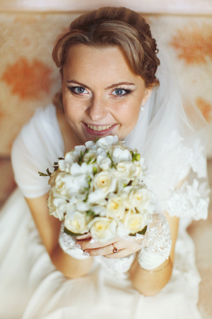 Pretty blue-eyed bride smiles over a bouquet of rosesの写真素材