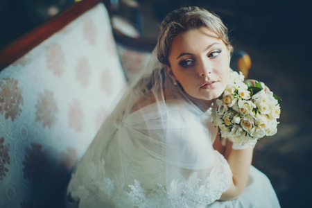 Bride in white laces looks old-fashioned while sits on the old sofaの写真素材