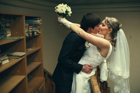 Man in black suit kisses a lady in white leaning her over the listの写真素材