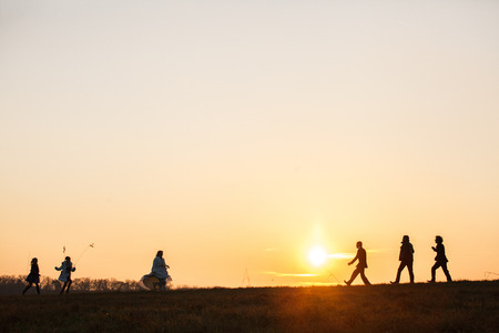 Bride and bridesmaids run towards groom and groomsmen over the field in the lights of sunsetの写真素材