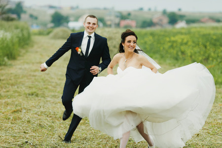 Bride runs away from groom on the fieldの写真素材