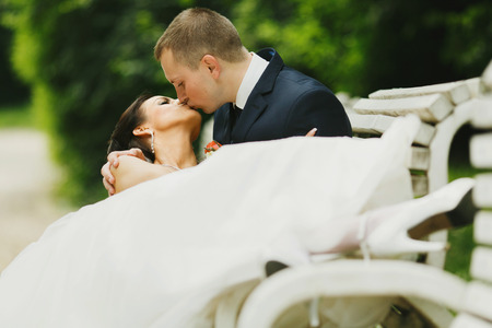 Groom kisses a bride while she lies in his hugs on the benchの写真素材