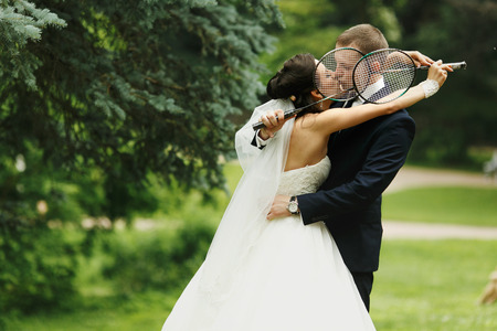 Bride and groom kiss hiding their faces behind the tennis-racketsの写真素材