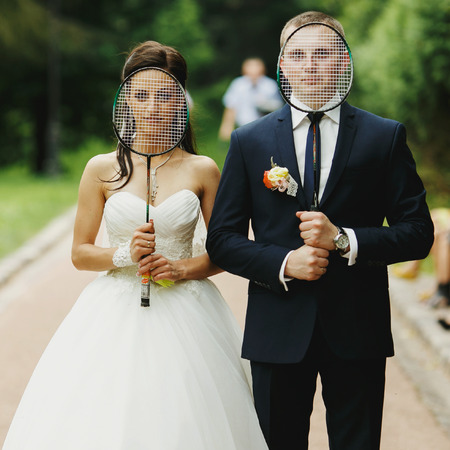 Bride and groom hide their faces behind tennis-racketsの写真素材