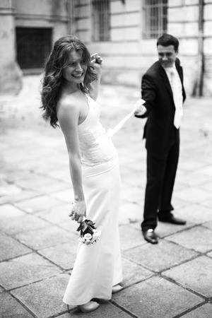 Groom holds a ribbon on bride's dress while she laughsの写真素材