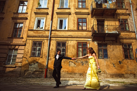 Groom holds bride's hand and pulls her along an old houseの写真素材