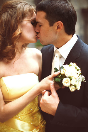 Groom kisses a bride while she holds a bouquet of white rosesの写真素材