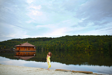 Barefooted woman in yellow dress stands on the lake's shoreの写真素材