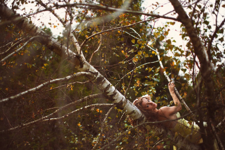 Woman in yellow dress lies on the tree branchの写真素材
