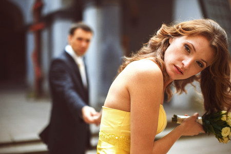 Bride in yellow dress looks thoughtful while she holds groom's handの写真素材