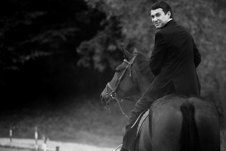 Man in black suit turns while he rides a horseの写真素材