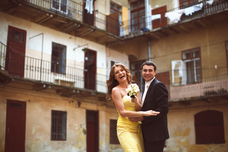 Bride laughs holding a bouquet of white roses and hugging with a groomの写真素材