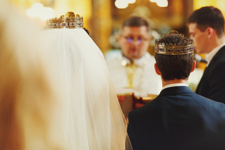 Bride and groom stand in the crowns before a priest during the engagement ceremonyの写真素材