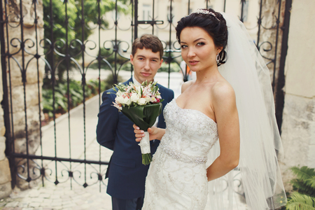 Bride and groom pose standing apart in the front of forged gatesの写真素材