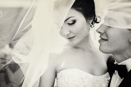 Bride looks down standing with a groom under veilの写真素材