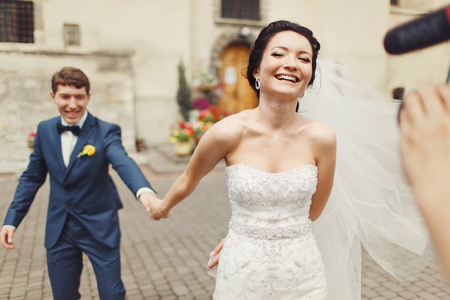 Bride holds groom's hand walking with him to the cameramanの写真素材