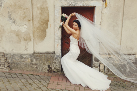 Bride stands behind an old door while wind blows away her veilの写真素材