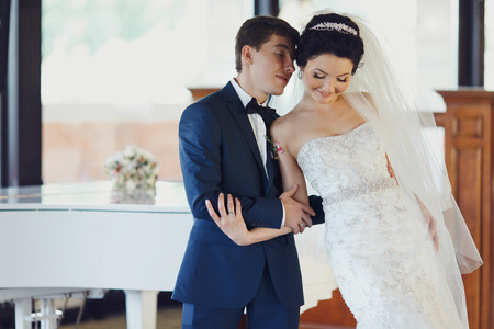 Bride leans on a groom's shoulder standing in the front of a pianoの写真素材