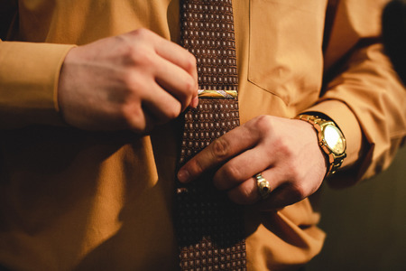 Man with a gold watch adjusts a tie