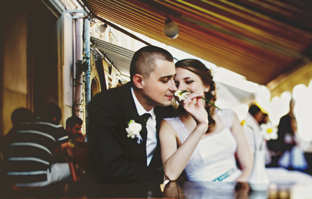 Groom smells a flower in the bride's hand while they rest in a street cafeの写真素材