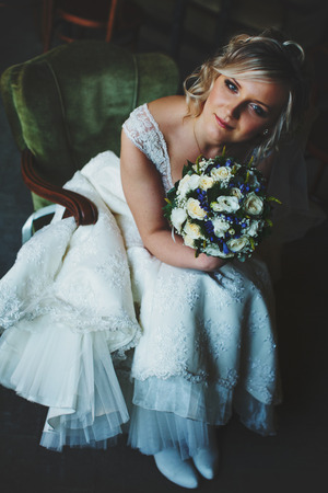 An attractive bride sits in vintage green chair holding a bouquetの写真素材