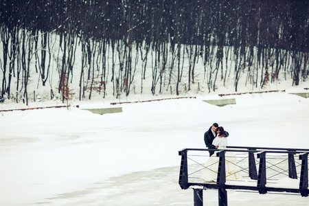 Bride and groom stand on the end of a bridge above the snowed up lakeの写真素材