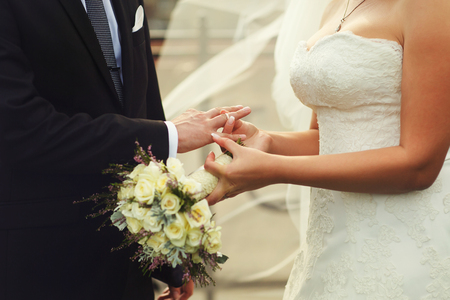 Bride delicately puts a wedding ring on groom's handの写真素材