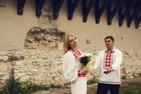 Bride in ethnic dress stands thoughtful behind an old wall while groom goes to herの写真素材