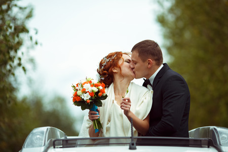 Happy newlyweds kiss standing in the car's hatchwayの写真素材