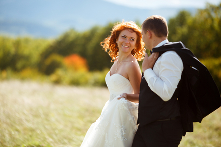 Bride looks with love at a groom walking along the fieldの写真素材