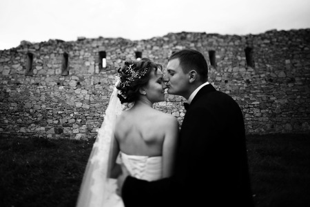 Groom kisses bride's nose standing in the front of an old wallの写真素材
