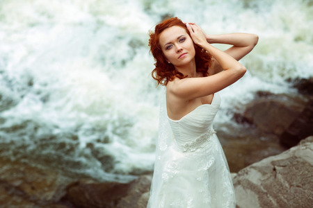 Bride looks gorgeous posing in the front of a foaming mountain riverの写真素材