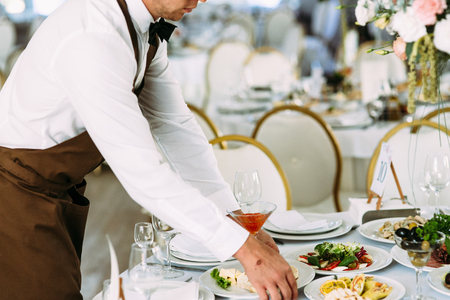 Waiter puts a plate with food on the tableの写真素材