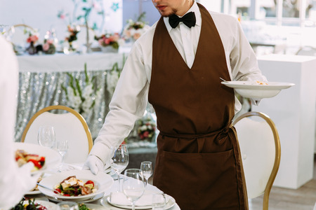 Wedding waiter is serving a table with mealsの写真素材