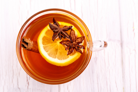 Cup of tea with cinnamon, lemon and other seasonings stands on white tableの写真素材