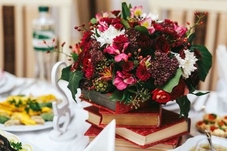 Rich autumn bouquet stands on a red books. Dinner table decorationの写真素材